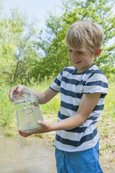 Deutschland, Bayern, München, Junge füllt Wasser in Glasgefäß am See, lächelnd - NH001402