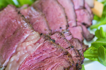 Sliced rib eye steak garnished with arugula and cantaloupe on plate, close up - ABAF000955
