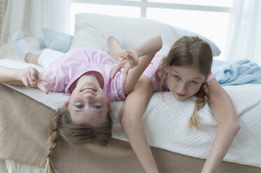 Germany, Bavaria, Portrait of girls lying on bed and showing V sign, smiling - CRF002438