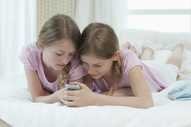 Deutschland, Bayern, Mädchen mit Smartphone auf dem Bett, lächelnd - CRF002439