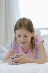 Deutschland, Bayern, Mädchen mit Smartphone auf dem Bett, lächelnd - CRF002440