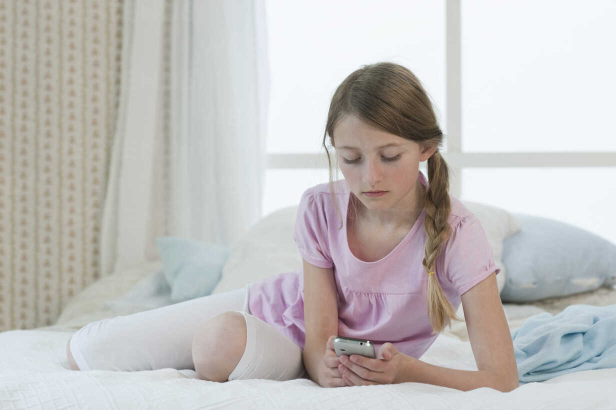 Little girl in underwear sitting on bed looking at smartphone