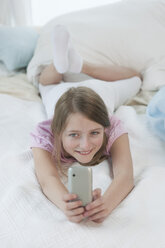 Deutschland, Bayern, Mädchen mit Smartphone auf dem Bett, lächelnd - CRF002443