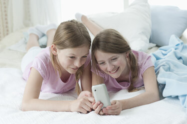 Deutschland, Bayern, Mädchen mit Smartphone auf dem Bett, lächelnd - CRF002444