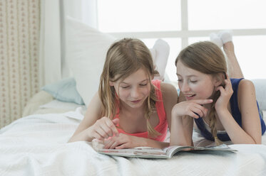 Deutschland, Bayern, Mädchen lesen Modezeitschrift auf Bett, lächelnd - CRF002447