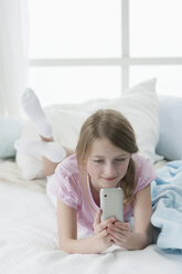 Germany, Bavaria, Girl using smart phone on bed, smiling - CRF002449