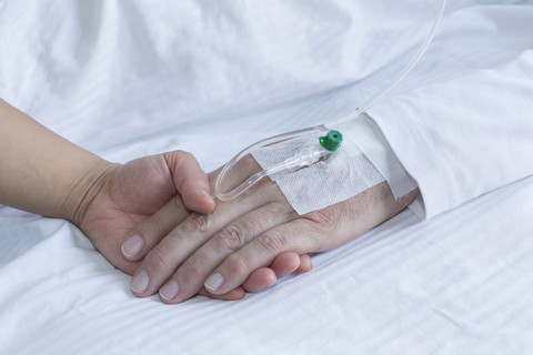 Deutschland, Freiburg, Frau hält Hand eines Mannes im Krankenhaus, Nahaufnahme, lizenzfreies Stockfoto