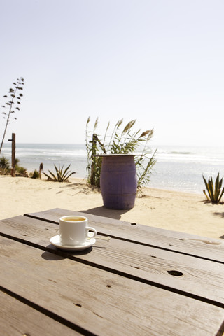 Spanien, Leere Cappuccinotasse am Meer, lizenzfreies Stockfoto