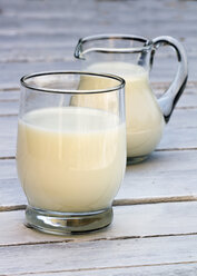 Glass of milk with milk jug on wooden table, close up - SARF000051