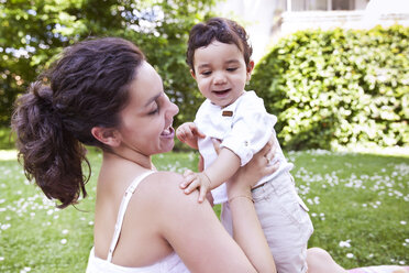 Mother cuddling her baby boy on grass, smiling - MFF000549