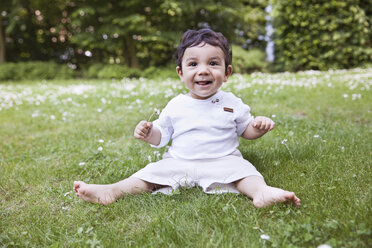 Baby boy sitting on grass and holding daisy flower, smiling - MFF000560
