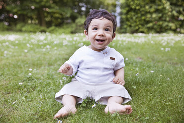 Baby boy sitting on grass and holding daisy flower, smiling - MFF000562