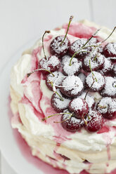 Pavlova with whipped cream, cherries, cherry sauce and icing sugar on cake stand, close up - EC000260