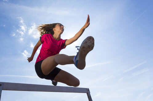 Germany, Young woman athlete jumping hurdles on track - STSF000076