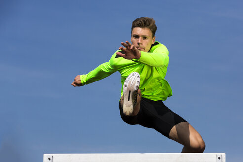 Germany, Man athlete jumping Hurdles on track - STSF000061
