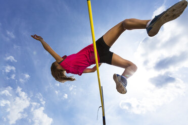 Germany, Young woman athlete jumping hurdles on track - STSF000079