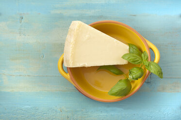 Bowl of parmesan cheese with basil on wooden table, close up - OD000239