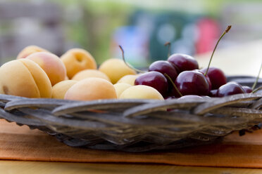 Germany, Bavaria, Landshut, Bowl of cherries and apricots on wooden table, close up - SAR000062