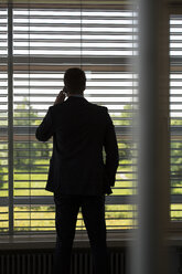 Germany, Hannover, Businessman talking on mobile phone in conference room - KFF000079