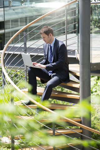 Deutschland, Hannover, Geschäftsmann sitzt auf Treppe und benutzt Laptop, lizenzfreies Stockfoto
