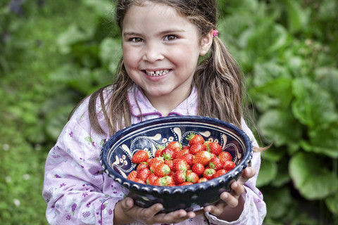 Deutschland, Nordrhein-Westfalen, Köln, Porträt eines lächelnden Mädchens, das eine Schale mit Erdbeeren hält, lizenzfreies Stockfoto