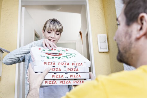 Deutschland, Nordrhein-Westfalen, Köln, Junge Frau nimmt Pizzakartons vom Pizzaboten, lächelnd - FMKYF000479
