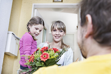 Deutschland, Nordrhein-Westfalen, Köln, Mutter und Tochter nehmen Blumen vom Postboten entgegen, lächelnd - FMKYF000510