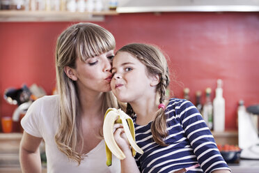 Germany, North Rhine Westphalia, Cologne, Girl eating banana while mother kissing - FMKYF000475