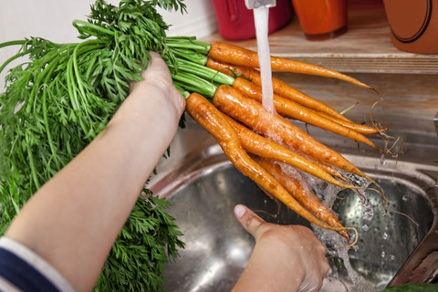 Deutschland, Nordrhein-Westfalen, Köln, Mädchen wäscht Karotten in Küchenspüle, Nahaufnahme, lizenzfreies Stockfoto