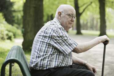 Germany, North Rhine Westphalia, Cologne, Senior man sitting on bench with walking stick in park - JAT000121