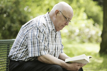 Deutschland, Nordrhein-Westfalen, Köln, Älterer Mann liest Buch auf Bank im Park - JAT000142