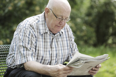 Deutschland, Nordrhein-Westfalen, Köln, Älterer Mann, der auf einer Bank im Park Zeitung liest - JAT000144