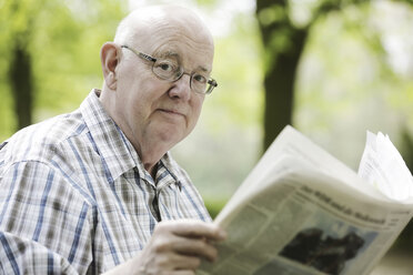 Deutschland, Nordrhein-Westfalen, Köln, Porträt eines älteren Mannes, der auf einer Bank im Park Zeitung liest - JAT000148