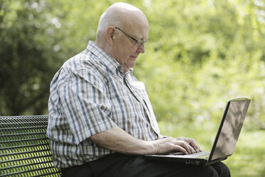 Germany, North Rhine Westphalia, Cologne, Senior man using laptop on bench in park - JAT000154