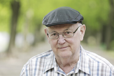 Deutschland, Nordrhein-Westfalen, Köln, Porträt eines älteren Mannes mit Mütze und Brille im Park, lächelnd - JAT000127