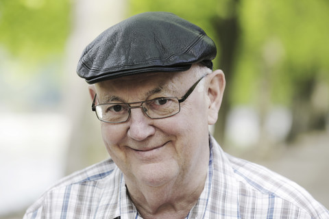 Deutschland, Nordrhein-Westfalen, Köln, Porträt eines älteren Mannes mit Mütze und Brille im Park, lächelnd, lizenzfreies Stockfoto
