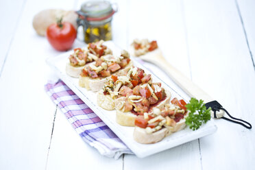 Teller mit Bruschetta mit Tomaten, weißen Shimeji-Pilzen, Kräutern und Olivenöl auf Holztisch, Nahaufnahme - MAEF007041