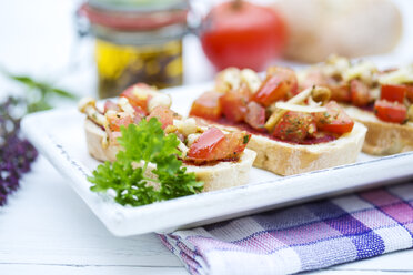 Plate of bruschetta with tomatoes, white shimeji mushrooms, herbs and olive oil on wooden table, close up - MAEF007102