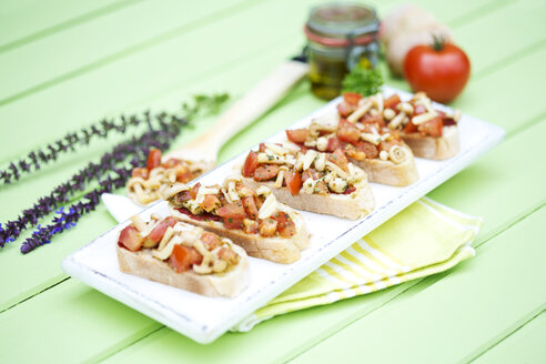 Teller mit Bruschetta mit Tomaten, weißen Shimeji-Pilzen, Kräutern und Olivenöl auf Holztisch, Nahaufnahme - MAEF007044