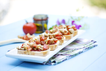 Teller mit Bruschetta mit Tomaten, weißen Shimeji-Pilzen, Kräutern und Olivenöl auf Holztisch, Nahaufnahme - MAEF007046