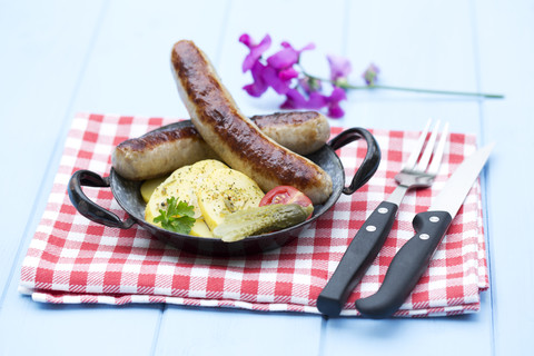 Bratwürste mit Kartoffeln und Essiggurke auf Holztisch, Nahaufnahme, lizenzfreies Stockfoto