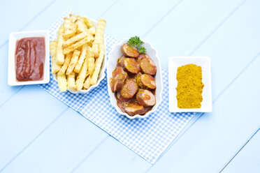 Bowl of sausages with french fries, currywurst and ketchup on wooden table, close up - MAEF007108