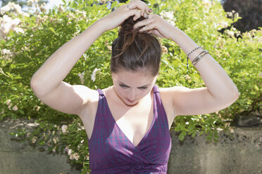 Germany, Bavaria, Munich, Young woman tying hair - TCF003513