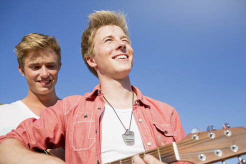 Germany, Two friends playing guitar in park - GDF000163