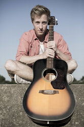 Deutschland, Junger Mann sitzt mit Gitarre an der Wand - GDF000180