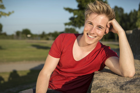 Deutschland, Junger Mann sitzt im Park, lächelnd, lizenzfreies Stockfoto