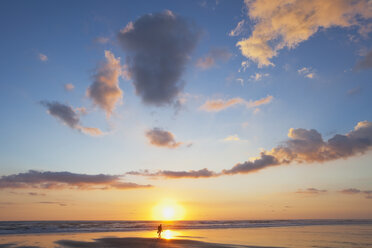 New Zealand, View of man carrying backpack walking along beach at sunset - GWF002355