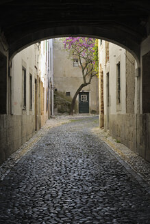 Portugal, Lissabon, Kleine kopfsteingepflasterte Straße durch einen Bogen - RUE001136