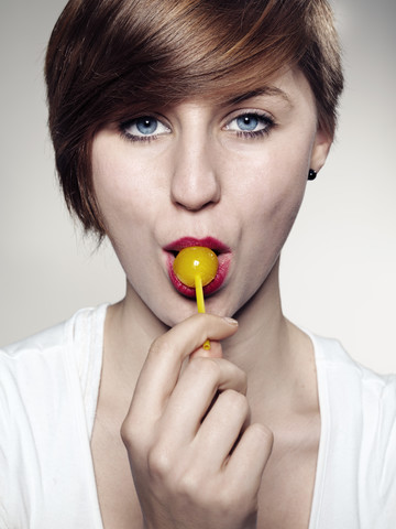 Porträt einer jungen Frau, die einen Lutscher hält, Nahaufnahme, lizenzfreies Stockfoto