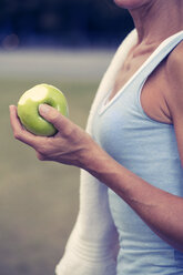 Sportive mature woman with towel around her neck holding apple, close-up - FKF000388